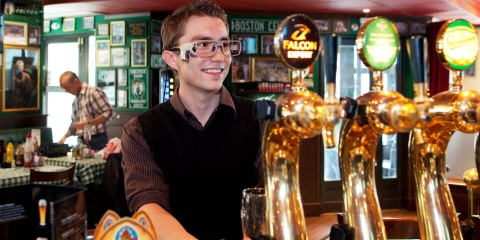 A young man wearing Tobii Pro Glasses eye tracker places an order in a bar.