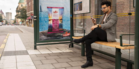 Man at a bus shelter looking at his mobile