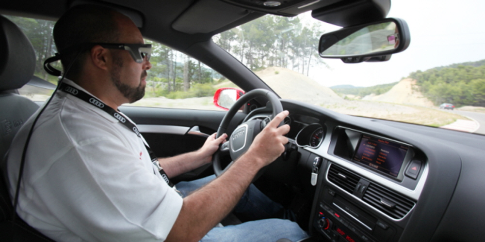 A man driving an Audi car wearing Tobii Pro Glasses eye tracker.