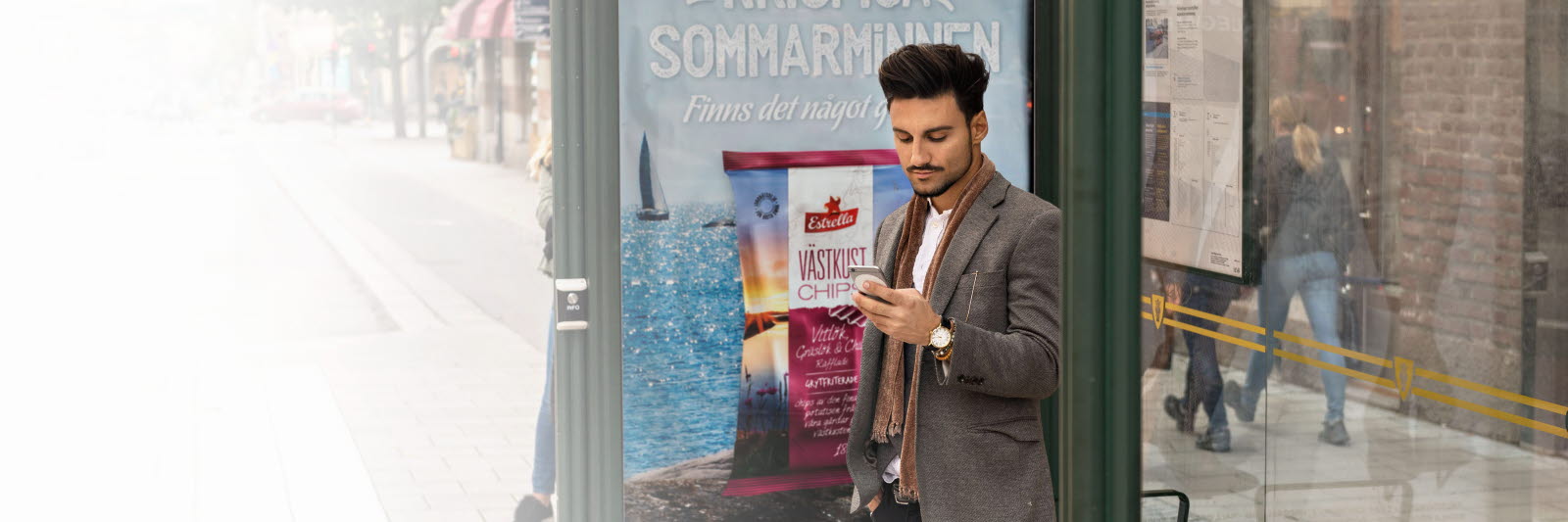 Man looking at mobile phone advertising at a bus stop
